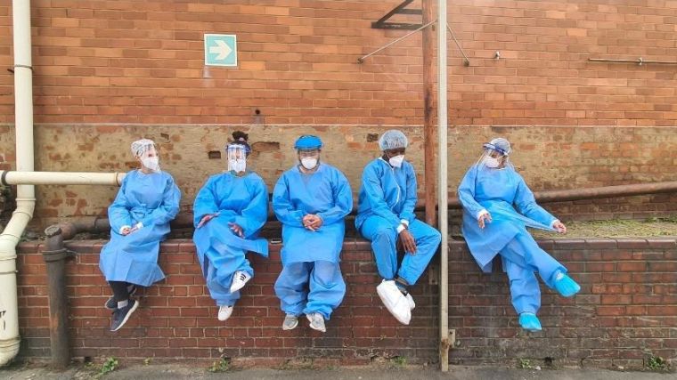 A group of medics sit on a wall wearing full protective equipment during the pandemic