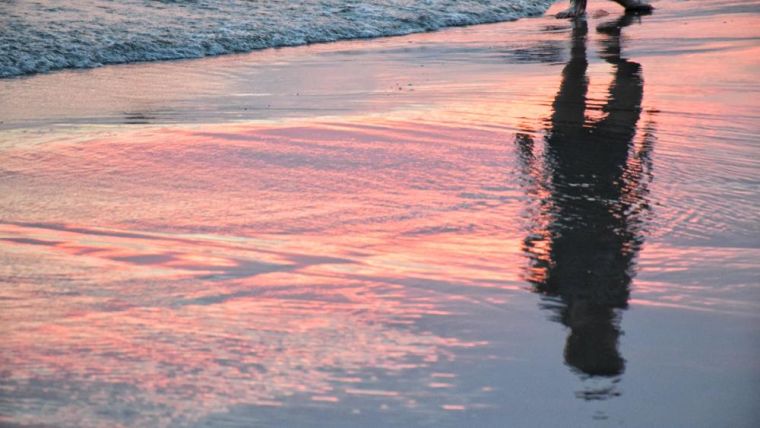A photo of a man and sunset sky reflected in the sea
