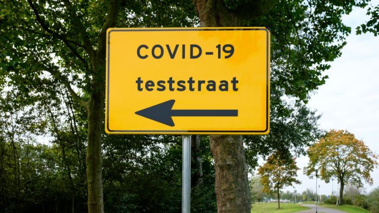 Amsterdam street sign showing direction to COVID-19 testing location. Translation of Dutch text on yellow sign: " COVID-19 teststreet".