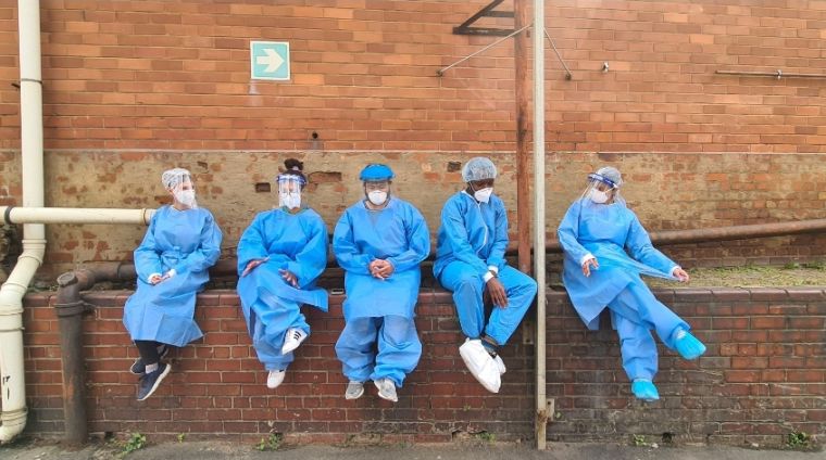 A group of medics sit on a wall wearing full protective equipment during the pandemic