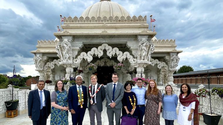 A group of people stand in front of Neasden Temple in London. Clouds are gathered in the background.