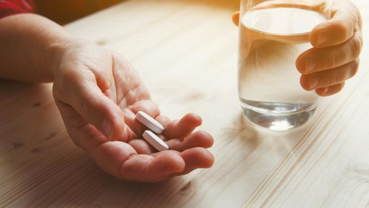 Image of a woman's hand with medication and a glass of water.