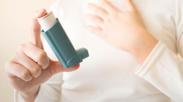 Young female in white t-shirt using blue asthma inhaler for relief asthma attack.